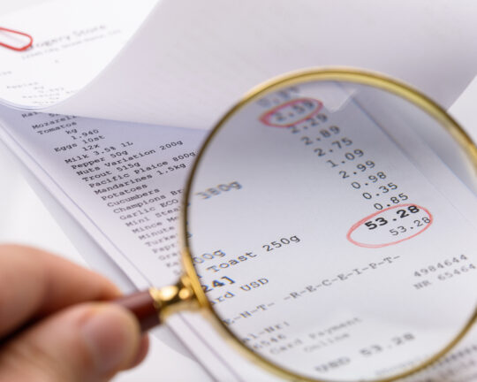 Magnifying glass examining a supermarket receipt with prices circled in red