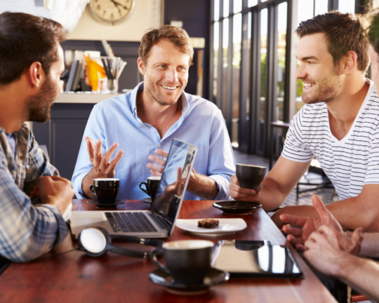 men sitting around a table with coffee and laptop
